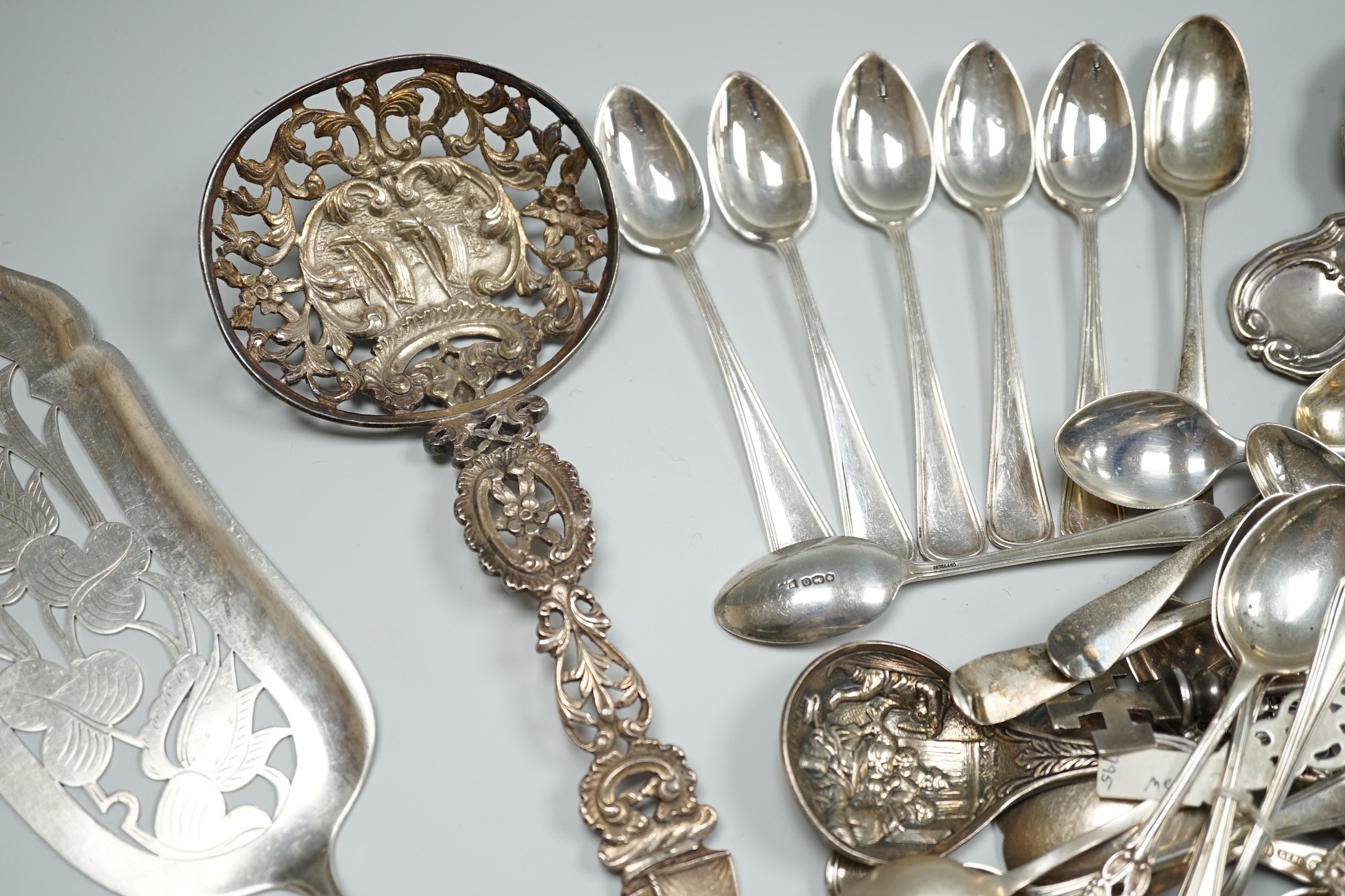 A group of mixed silver and white metal items including flatware, Dutch fish slice, German 800 tea strainer, George IV 'Claret' wine label, etc. and a plated spoon.